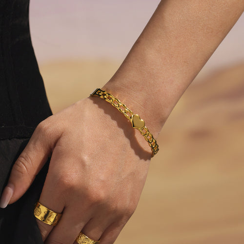 Single gold heart link clasp bangle worn on wrist outdoors