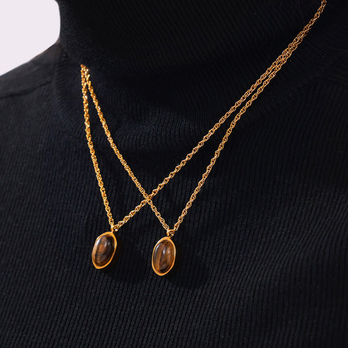 Two gold tiger-eye oval pendants worn crossed on black turtleneck