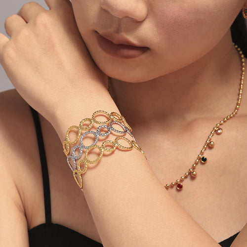 Stacked gold and silver twisted link cuffs on one wrist