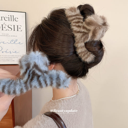 Brown fur claw clip in hair bun with blue clip held in hand