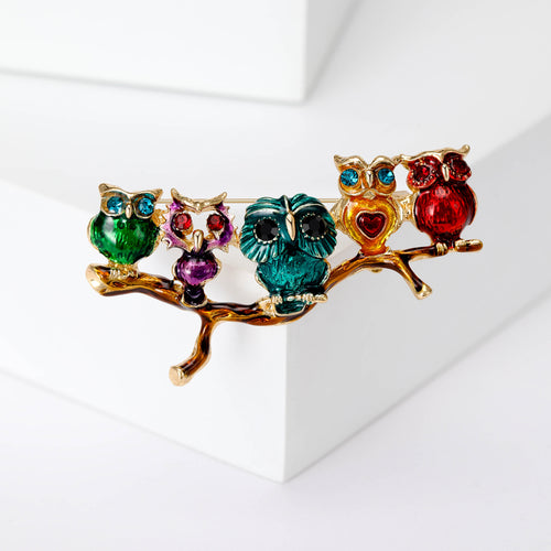 Five small jeweled owls perched together on a branch shown in a styled display.