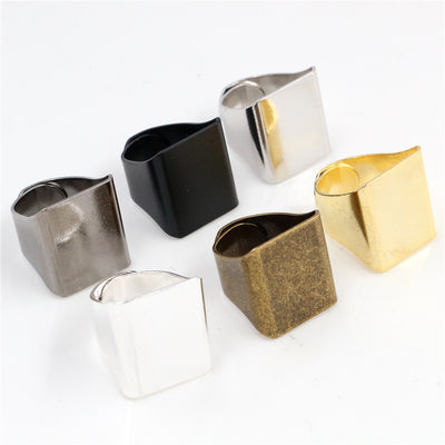Assorted square top ring blanks in gold, silver, black, and bronze tones arranged together on a plain background