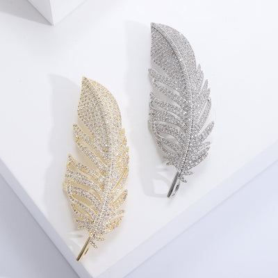 Gold and silver pave crystal feather brooches side by side on white blocks