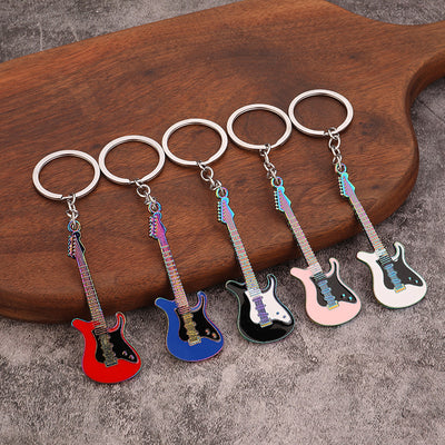 Five electric guitar keychains in red, blue, black, pink and white displayed on a wooden board.
