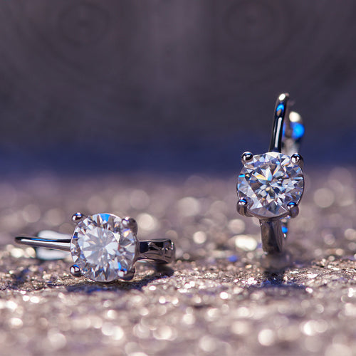 Pair of round clear stone huggies on glittery surface blue light