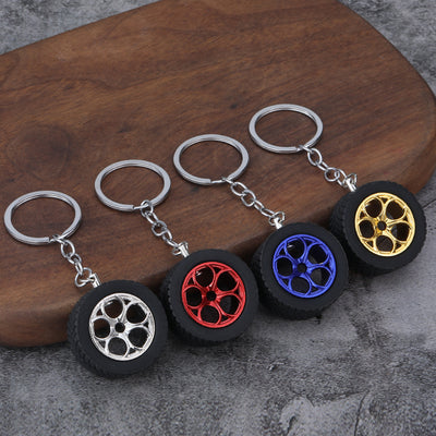 Four tire wheel keychains with silver, red, blue, and gold rims on a wooden surface.