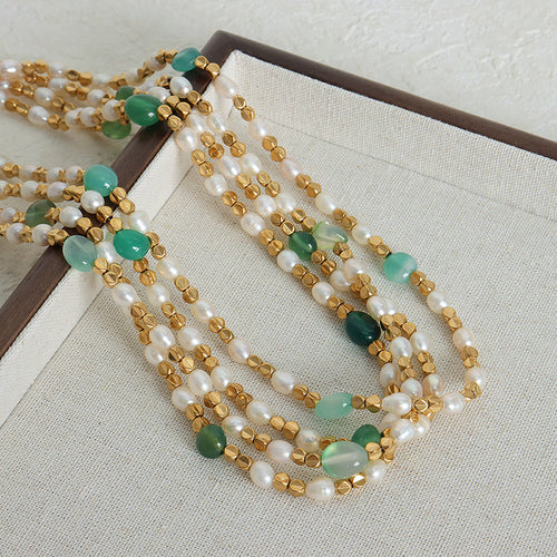 Multiple gold pearl green stone bead necklaces coiled on fabric tray