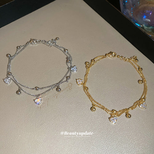 Silver and gold double-layer heart charm bracelets laid on beige surface