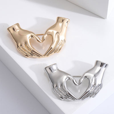 Gold and silver heart hands gesture brooches displayed together