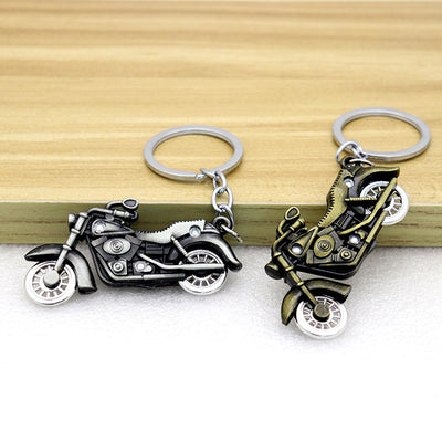 Two motorcycle keychains in antique silver and bronze tones rest on a wooden ledge.