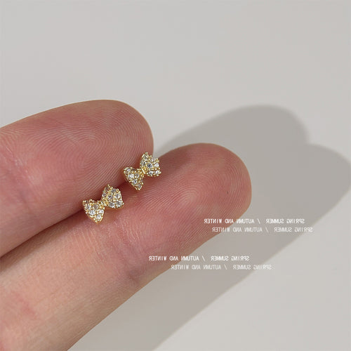 Gold-tone clear-stone tiny-bow studs shown worn on an ear.
