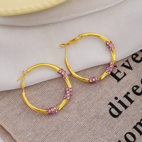 Gold twisted purple crystal hoops on white fabric over burlap