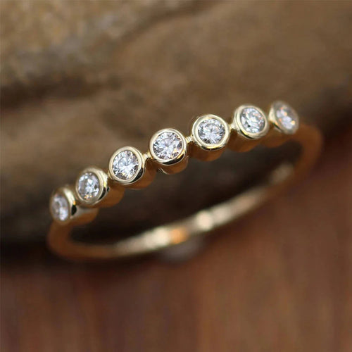 Gold seven-stone bezel thin band ring on rock wood background