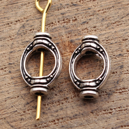 Open oval connector with dotted border details and loops at both ends displayed on a natural wood setting