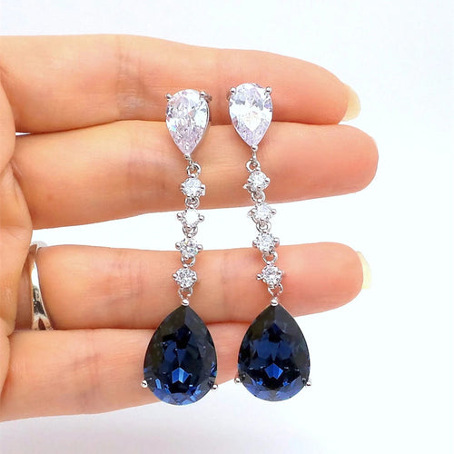 Silver clear and blue teardrop long drop earrings held across fingers