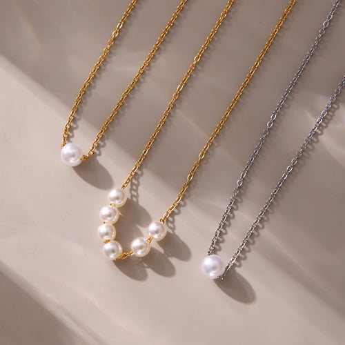 Gold and steel single-pearl and five-pearl necklaces on beige surface