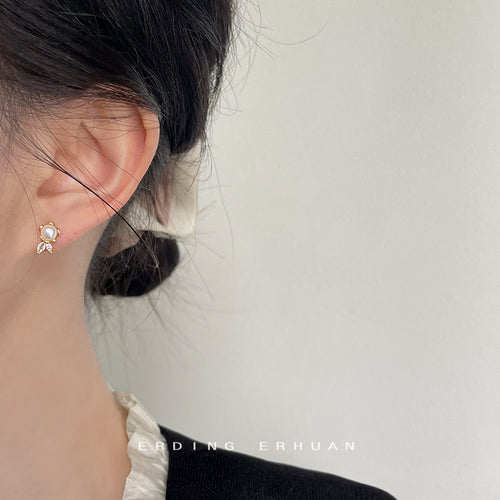Gold-tone white-pearl-flower clear-leaf studs shown worn on an ear.