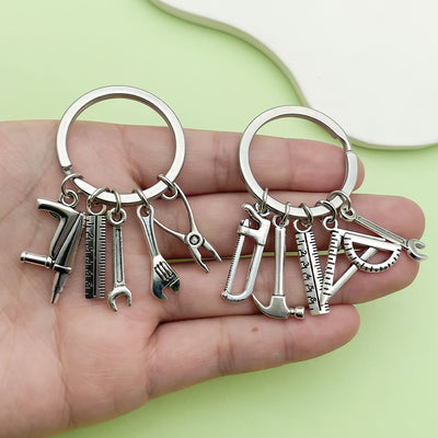 A hand holds two silver-tone keychains with assorted miniature tool charms.