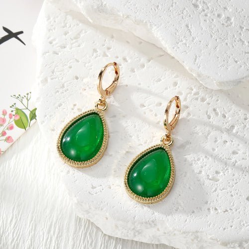 Pair of green teardrop lever-back hoop earrings on white stone prop