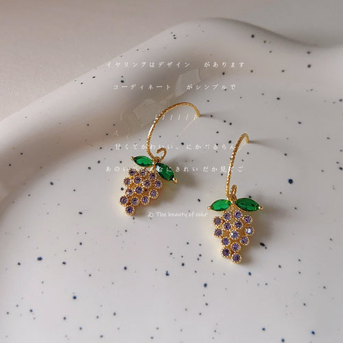 Gold purple zircon grape cluster earrings on speckled white plate