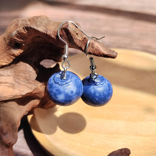 Pair of mottled blue blueberry resin earrings on silver hooks by wood