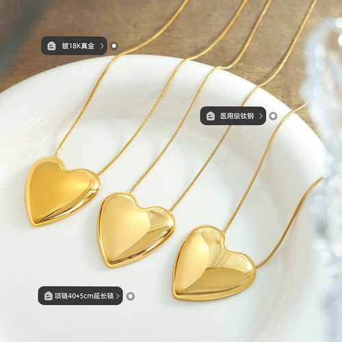 Three gold heart pendants on white dish with material labels