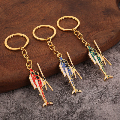 Three helicopter keychains in red, blue, and green displayed on wood and gray fabric.