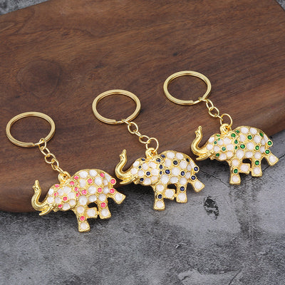 Three elephant keychains with pink, dark blue, and green accents on a wooden backdrop.