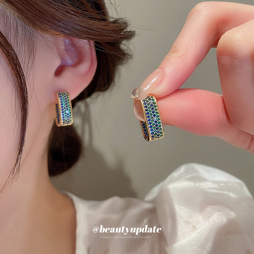 Styled close-up of green crystal geometric hoop earrings