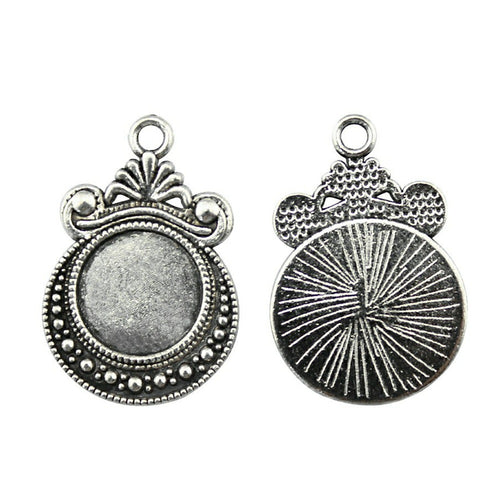 Ornate Round Cabochon Pendant Settings in Two Finishes arranged on a wood slice