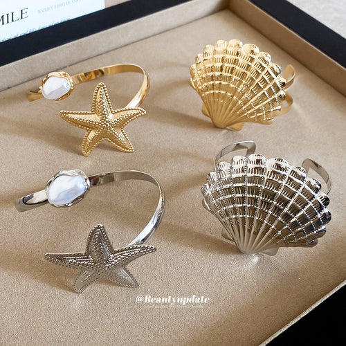 Four open cuffs in tray: gold and silver shells and starfish with pearls