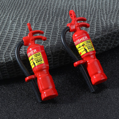 Two red fire extinguisher charms with black hoses and yellow warning labels on a dark textured surface