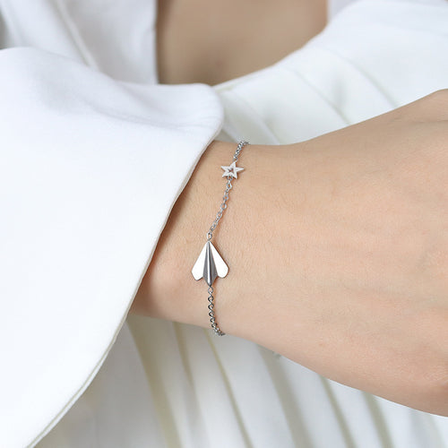 Silver paper airplane and star bracelet worn on wrist with white sleeve