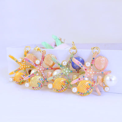 Four jeweled starfish and seashell ornaments are arranged together on a white surface.