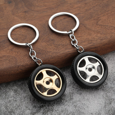 Two car wheel keychains with gold and silver five-spoke centers on wood and gray fabric.
