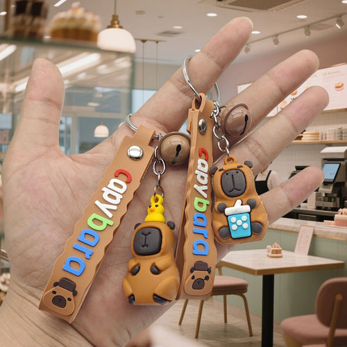 Two capybara keychains duck hat and bubble tea held in cafe