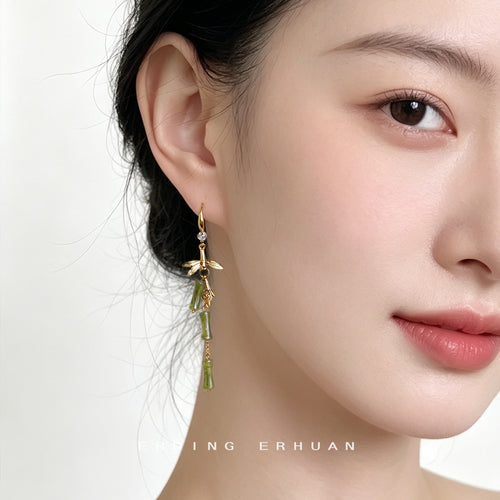 Gold-tone green-bamboo-branch long-hook earrings shown worn on an ear.