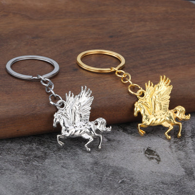 Two Pegasus keychains in silver and gold tones displayed on wood.