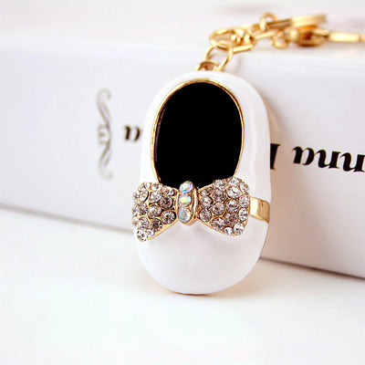 Close-up of a white shoe charm with a black interior, clear rhinestone bow, and gold-tone hardware.