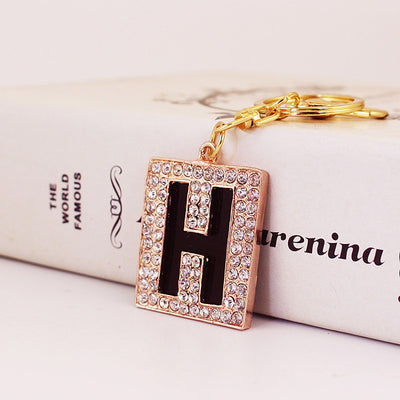 Close-up of a black letter H charm framed by clear rhinestones beside a gold-tone key ring.