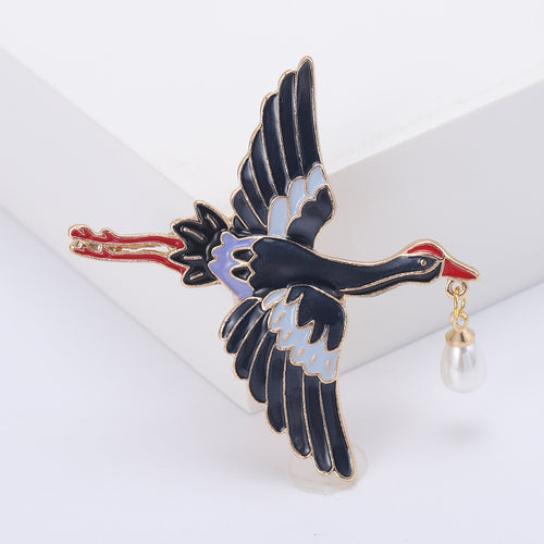 Angled display of flying crane with spread wings and a suspended white pearl-like drop