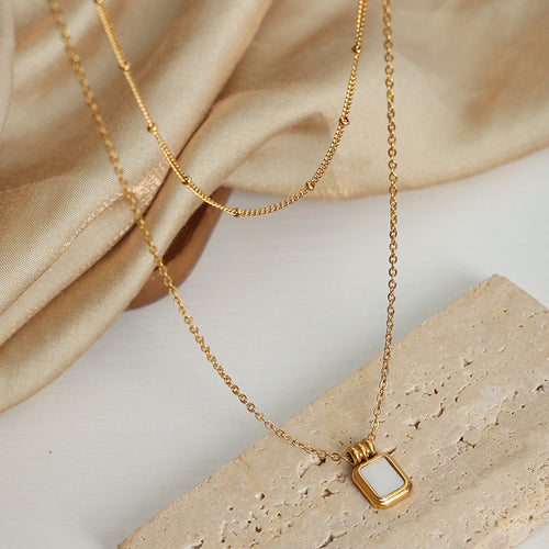 Gold shell pendant necklace flat on stone with silk fabric