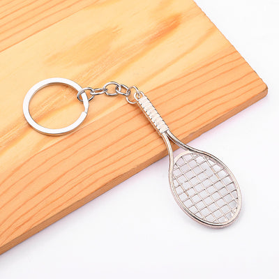 Silver tennis racket key ring resting on a wooden board.