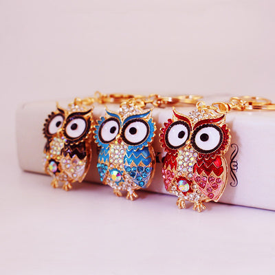 Three gold-tone owl keychains in black, blue, and red displayed side by side.