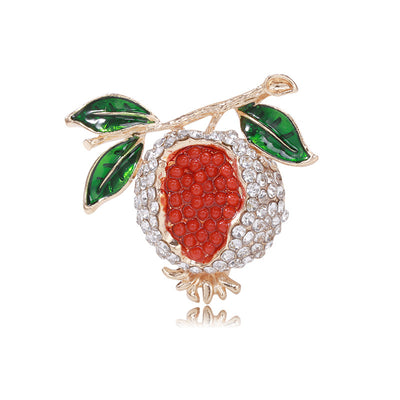 Front view of red pomegranate framed by clear stones, green leaves, and a gold-tone branch
