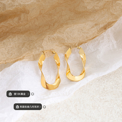 Pair of gold twisted open hoop earrings on crumpled paper with caption tags