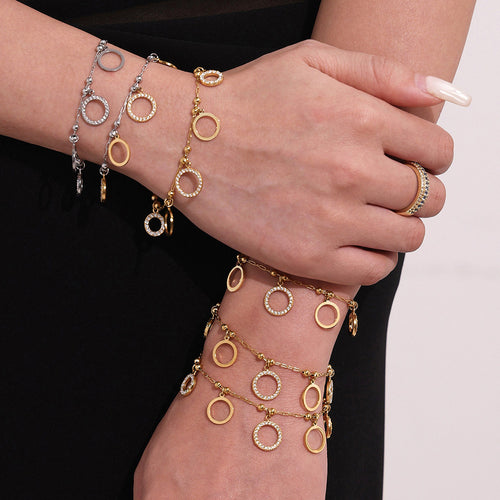 Model wearing stacked gold and steel circle charm bracelets on both wrists