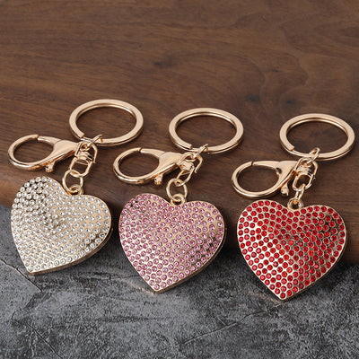 Three heart keychains covered in clear, pink, and red rhinestones on a wooden surface.