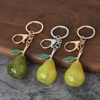 Three glitter pear keychains in yellow and green with two hardware finishes on a wooden surface.