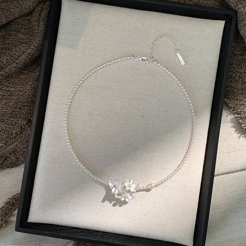 Front view of white pearl strand necklace with floral center accent